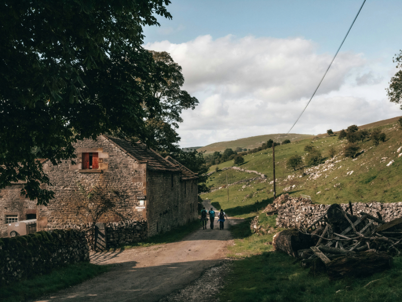People walking down dirt road in hills next to old farm building