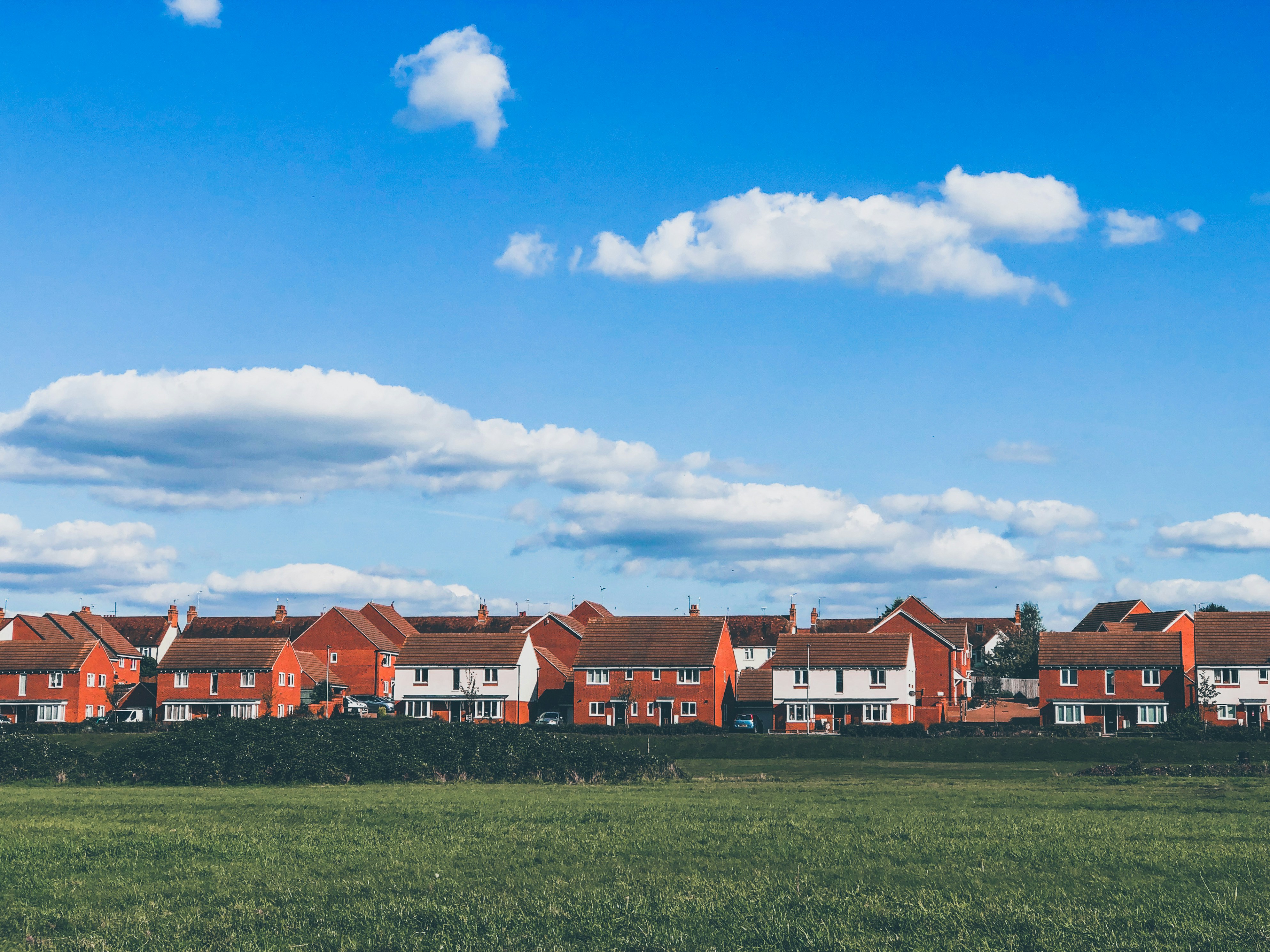 Houses in front of green field under blue sky with clouds