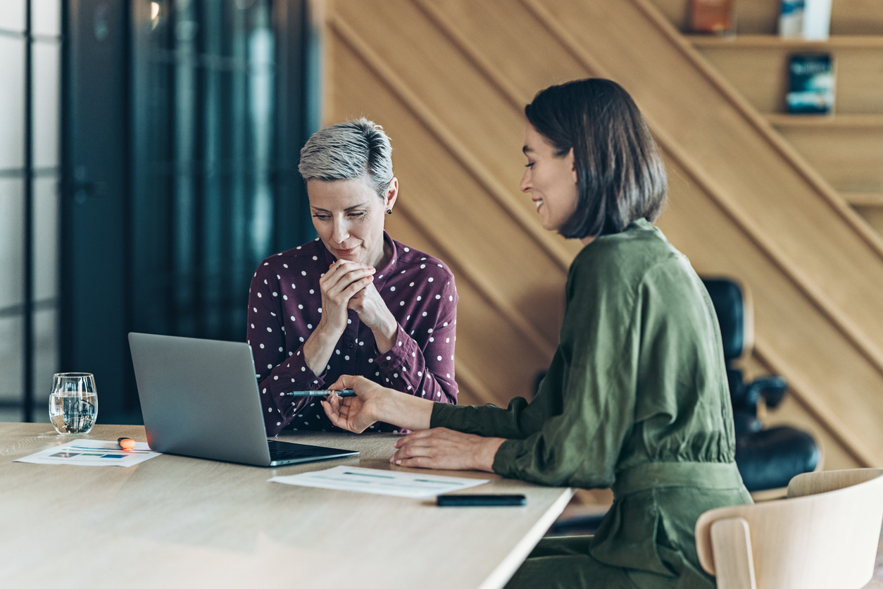  
Two women sitting at table looking at a laptop
