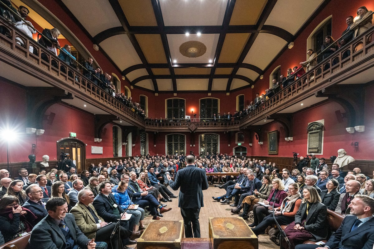 a man addressing an audience in a red hall